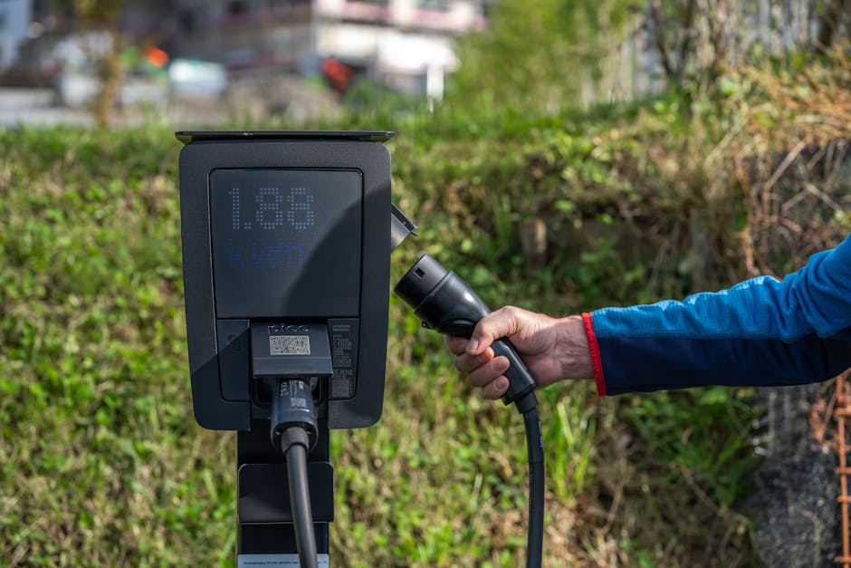 An outdoor electric car charging station with a hand holding a charging cable.