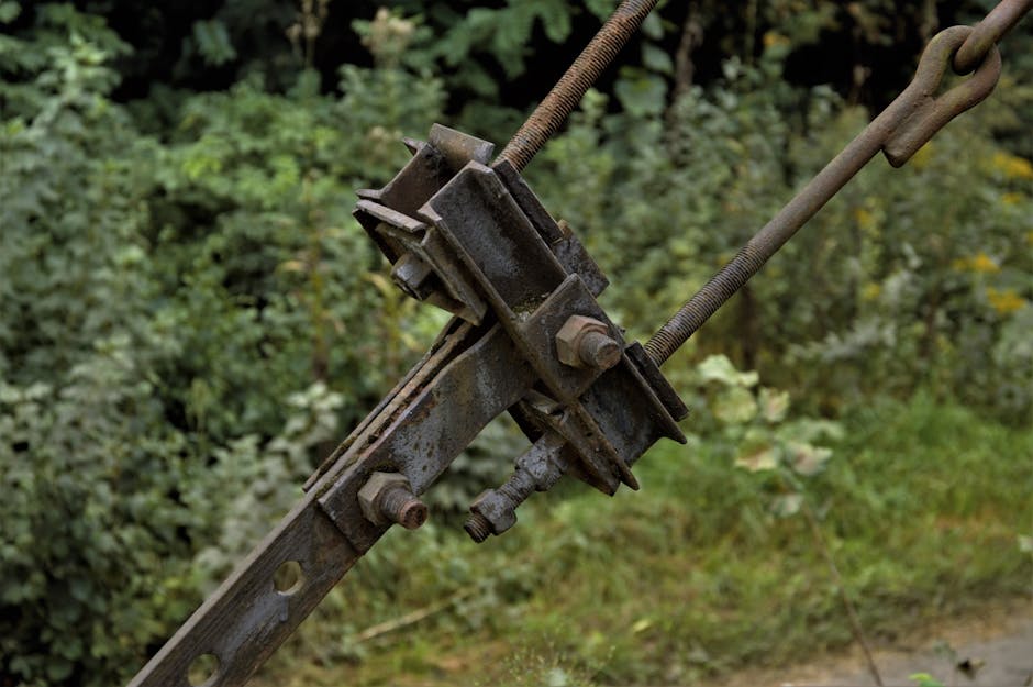 Close-up of a weathered metal clamp in a lush, outdoor industrial setting.