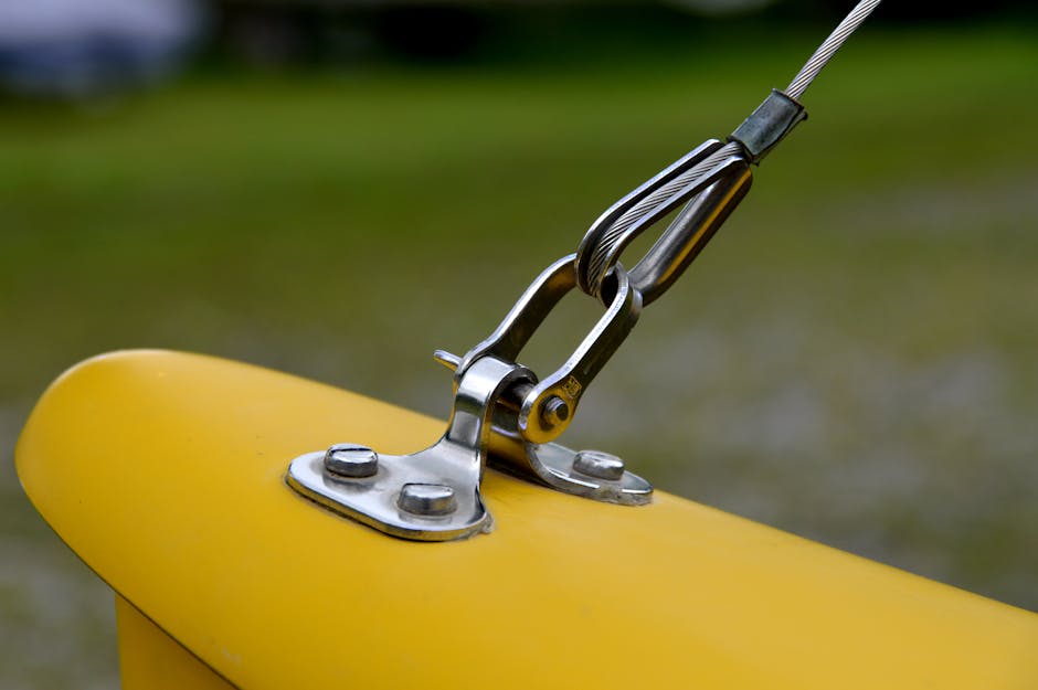 Detailed view of a metal wire rope fastened to a bright yellow surface outdoors.