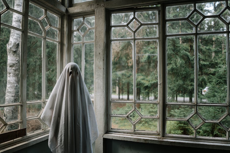 Ghost sheet costume in rustic room overlooking a forest, creating a spooky vibe.