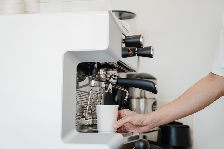 Person's hand using an espresso machine to prepare coffee. Modern kitchen setting.