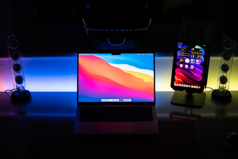 Stylish workspace featuring a colorful laptop and tablet with ambient lighting.