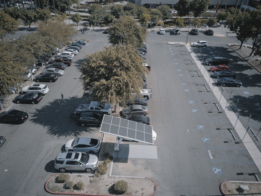 Aerial view of a solar panel charging station in a busy parking lot surrounded by cars and trees.