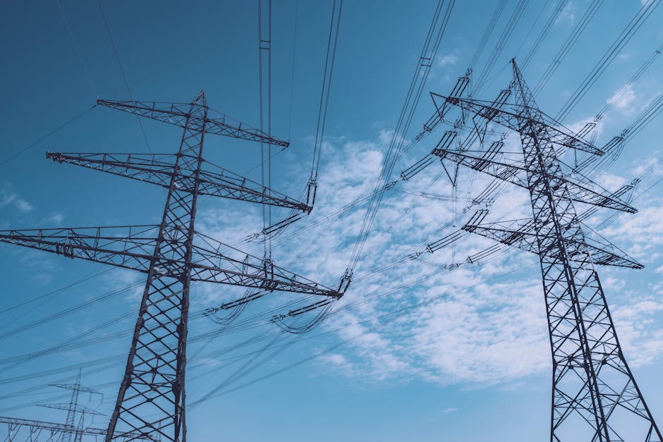 High voltage transmission towers stretch across a clear blue sky, symbolizing energy and industry.