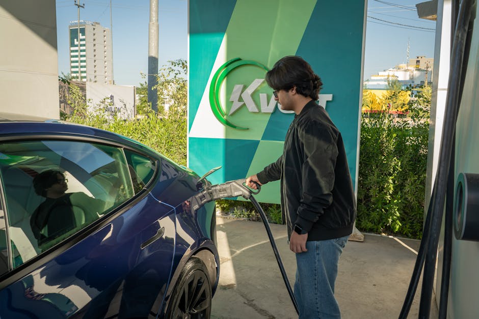 Young man charging a Tesla Model 3 at an outdoor electric vehicle station during the day.
