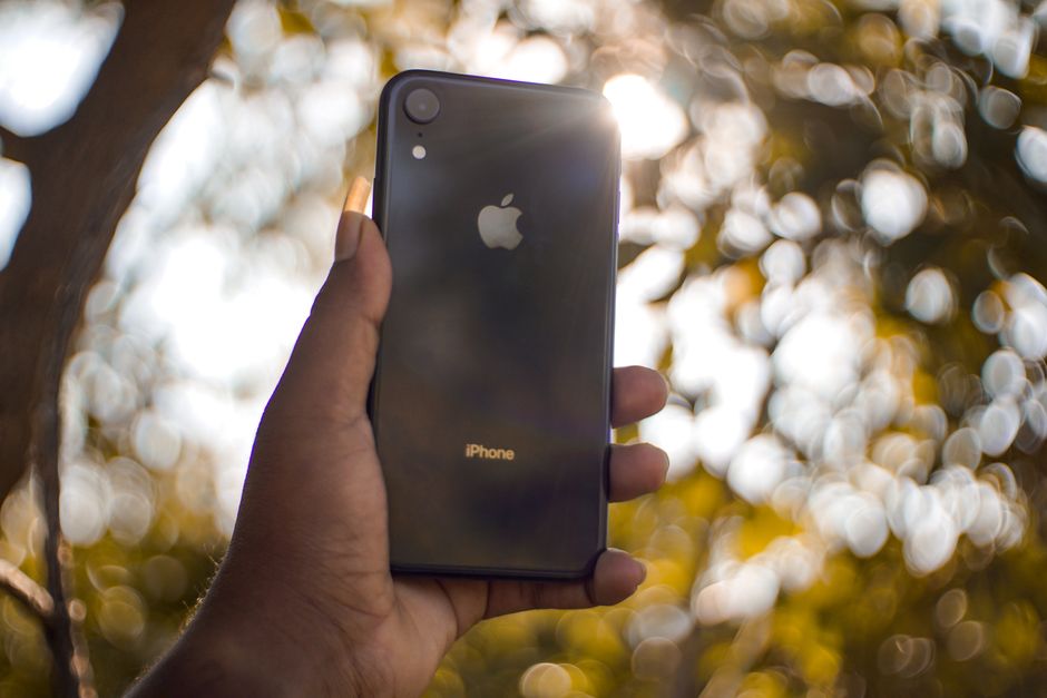A hand holding a smartphone outdoors with bokeh effect in the background.