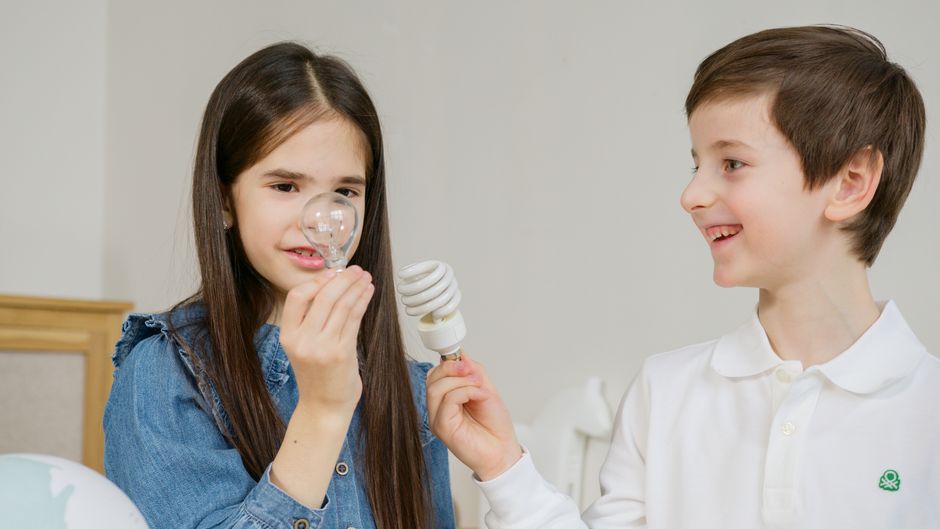 Two children learning about energy efficiency with lightbulbs indoors.