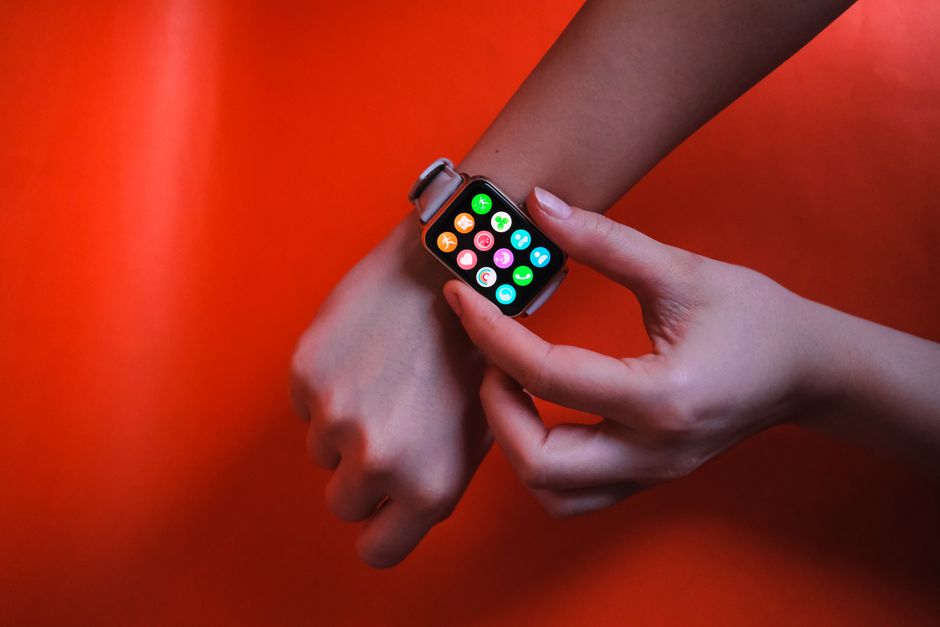 A close-up image of hands interacting with a smart watch against a vibrant red background, highlighting modern technology and connectivity.