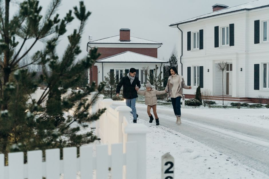 A cheerful family enjoys a winter walk in front of a beautiful suburban home during a snowy day.