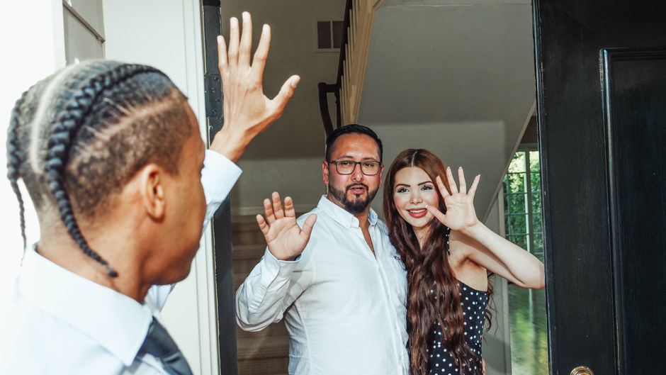 A couple welcoming a guest at their new home, symbolizing hospitality and new beginnings.