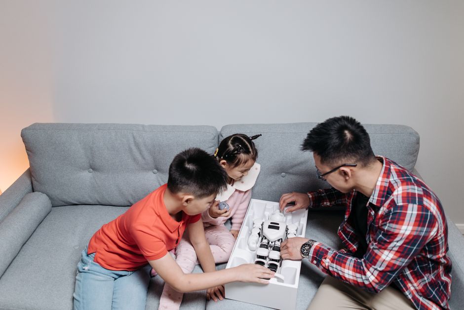 A family with children bonding over assembling a robot toy on a living room couch.