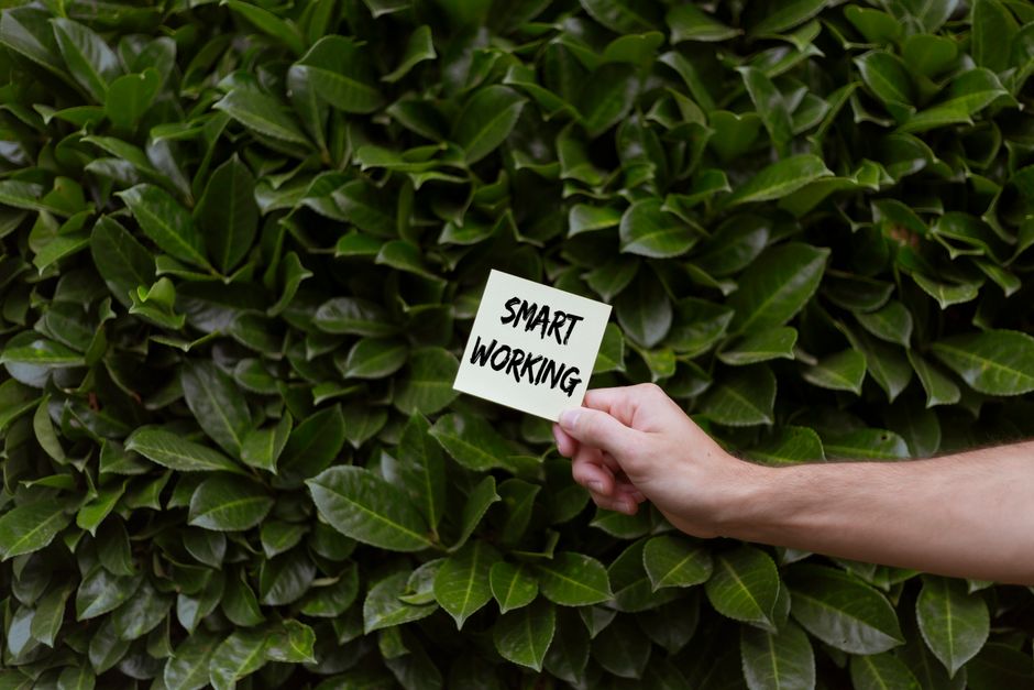 A hand holds a note with 'Smart Working' text against a lush green background.