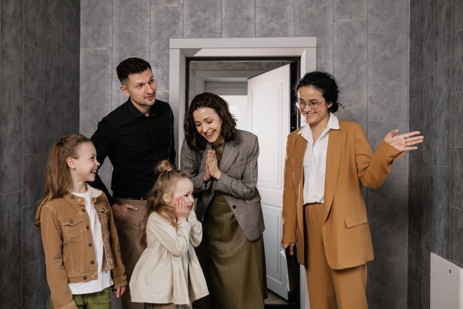 A joyful family is warmly welcomed by a realtor inside a modern home.
