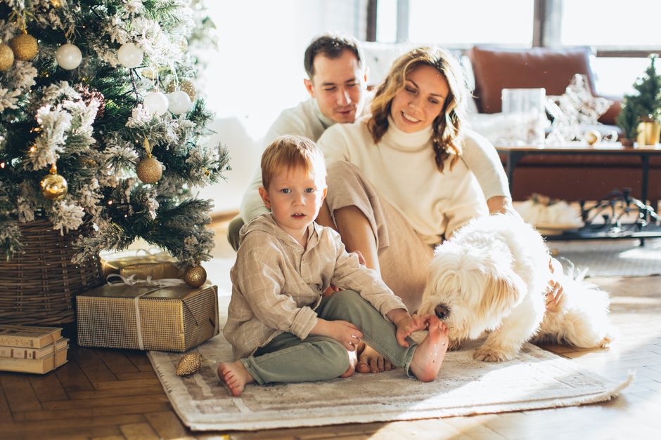 A joyful family with their pet dog celebrates Christmas morning at home by the tree.