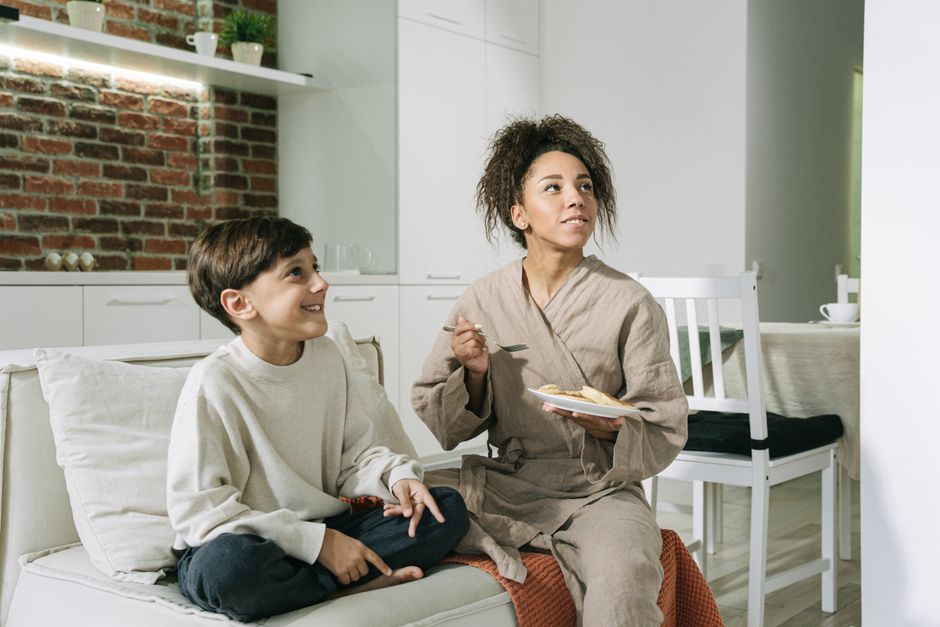 A mother and son enjoy a cozy breakfast on the couch at home, fostering love and togetherness.