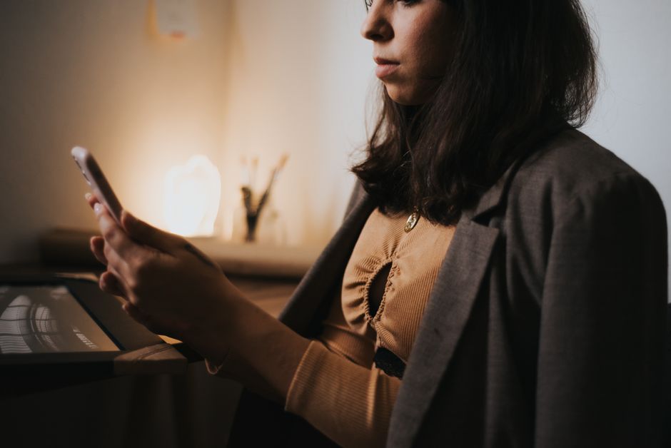 A stylish woman using a smartphone in an intimate home office, wearing a suit jacket.