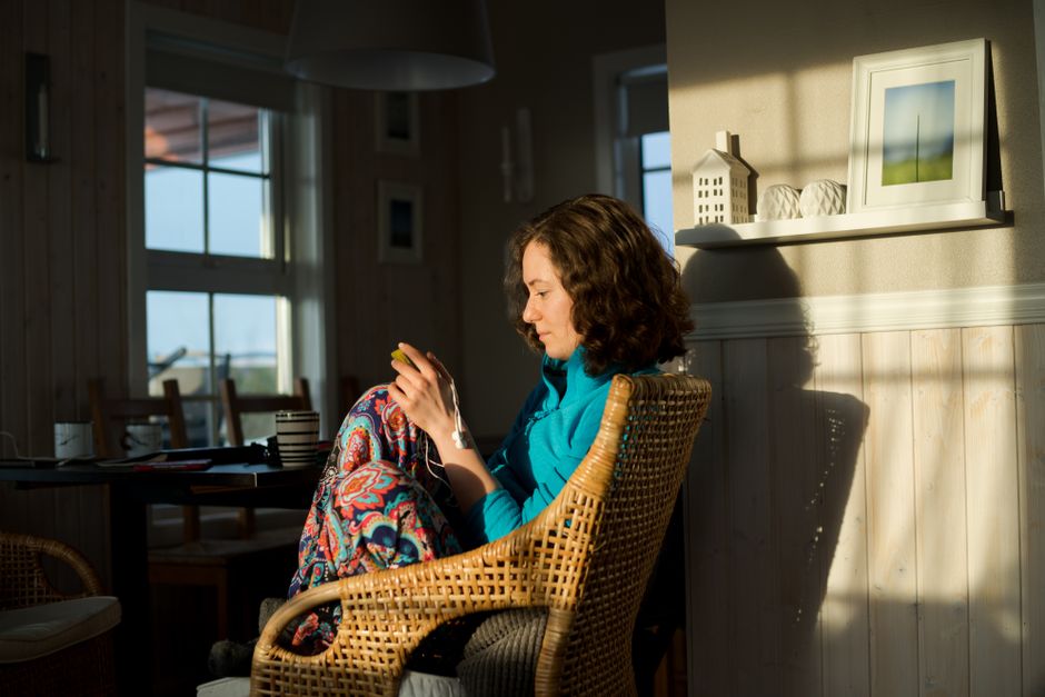 A woman enjoying a peaceful moment indoors, sitting in a sunlit rattan chair, surrounded by artistic home decor.