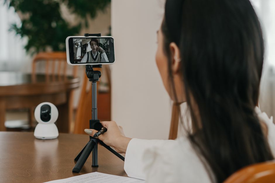 A woman making a video call on a smartphone using a cellphone stand indoors.