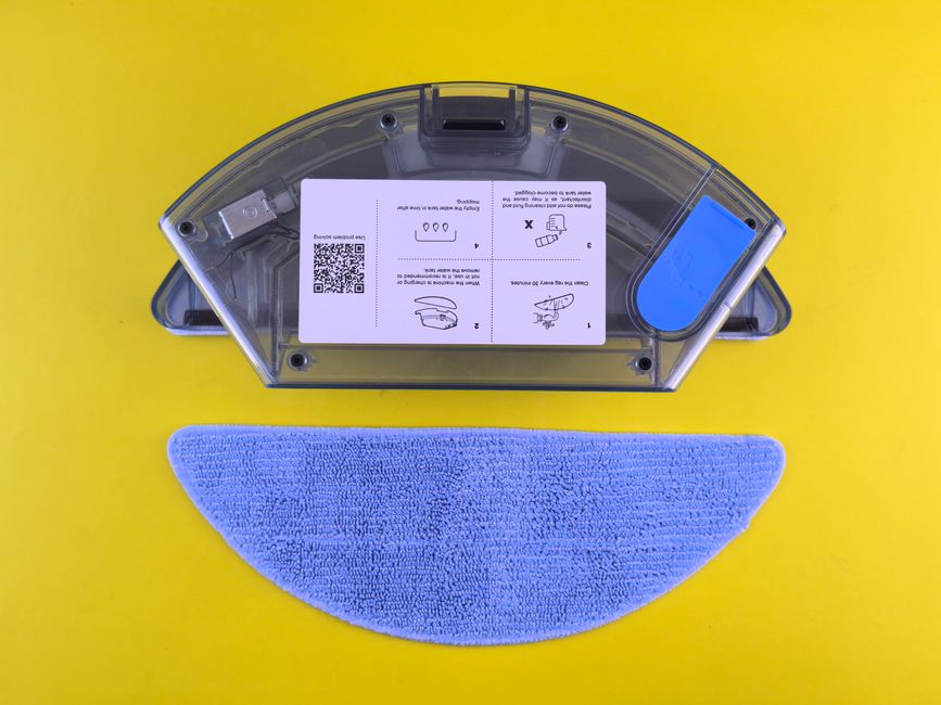 Cleaning robot water tank and mop on yellow backdrop, showcasing household appliance detail.