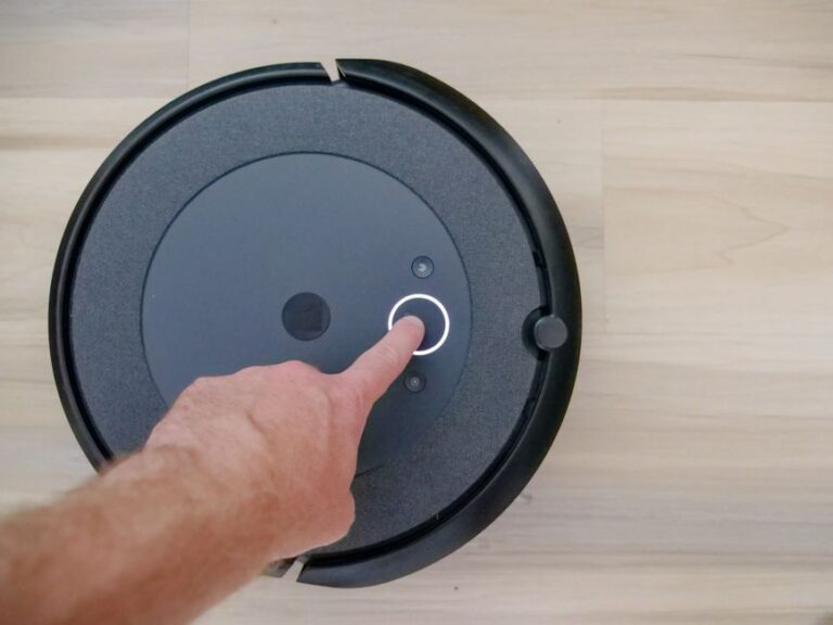 Close-up of a finger pressing a start button on a robotic vacuum cleaner at home.
