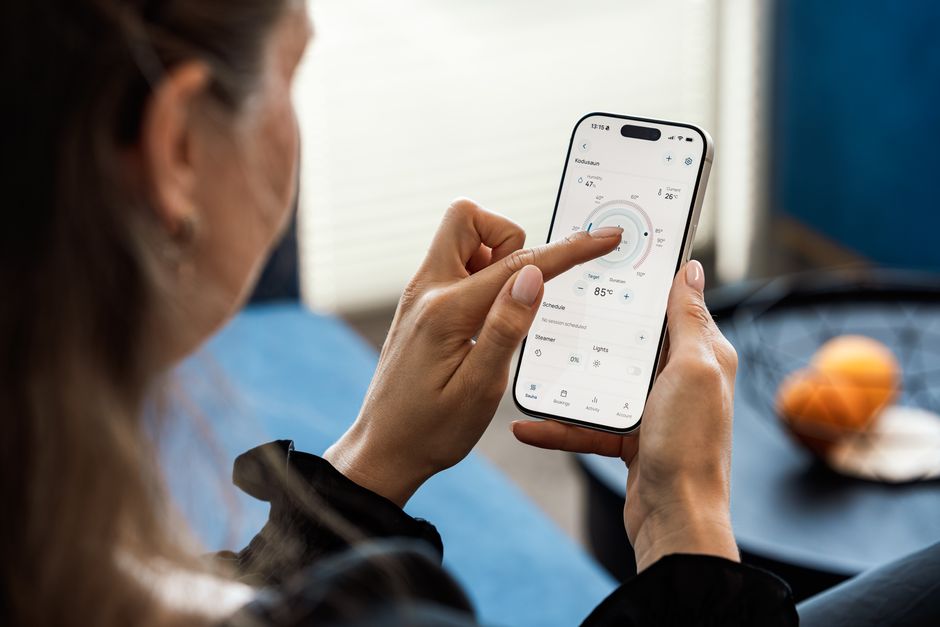 Close-up of a woman using a smartphone app to control sauna settings, indoors.