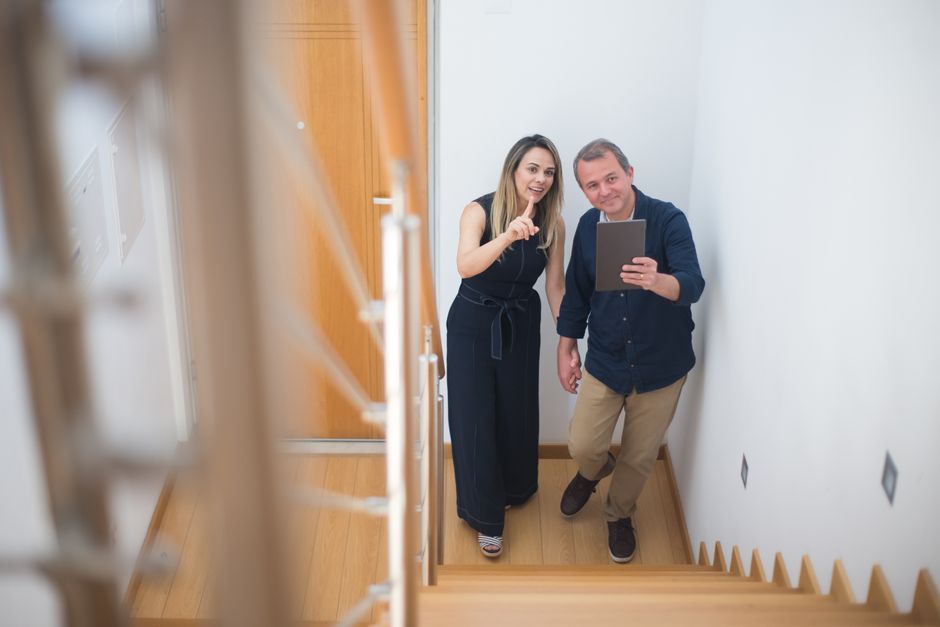 Couple taking a selfie in a new home, enjoying interior design on wooden stairs.