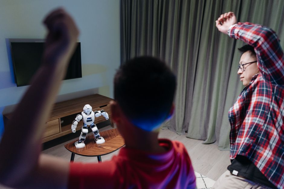 Father and son dancing enthusiastically with a toy robot at home, enjoying family time together.