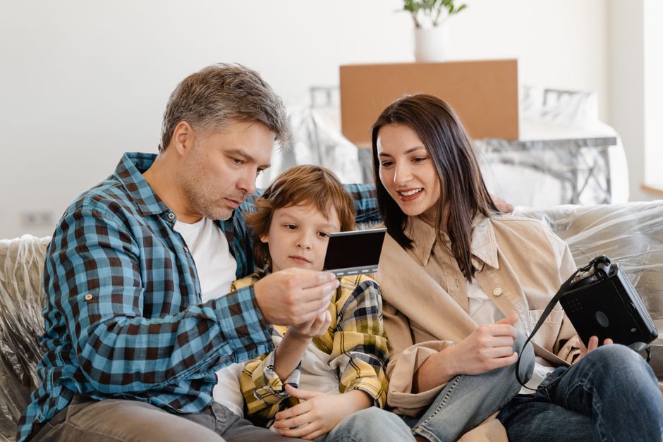 Happy family sitting on couch looking at instant photo in their new home.