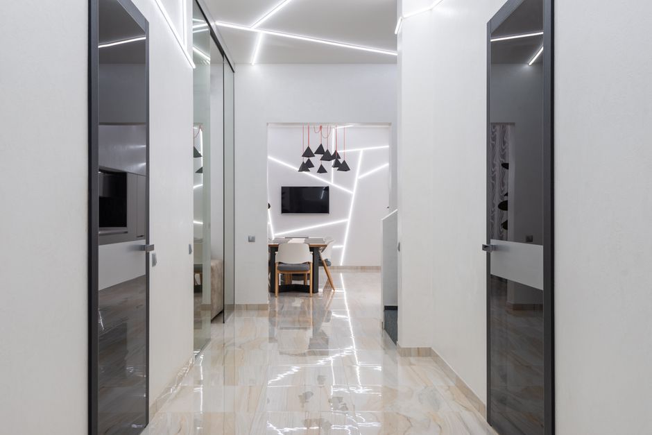 Interior of empty spacious hallway in house with glass doors and white walls near table with chairs next to TV under lamps