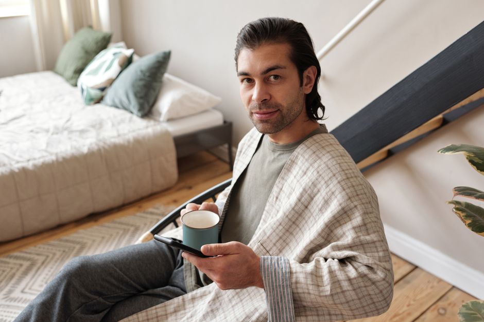 Man in a comfortable home setting enjoying a cup of coffee while relaxing with a mobile device.
