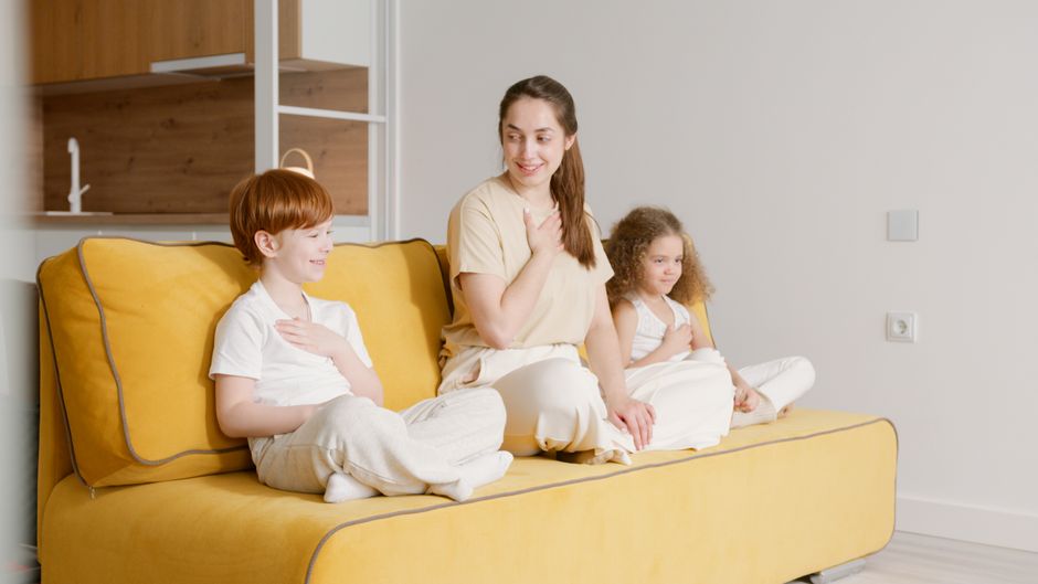 Mother and children sitting together on a yellow sofa at home, enjoying quality time.