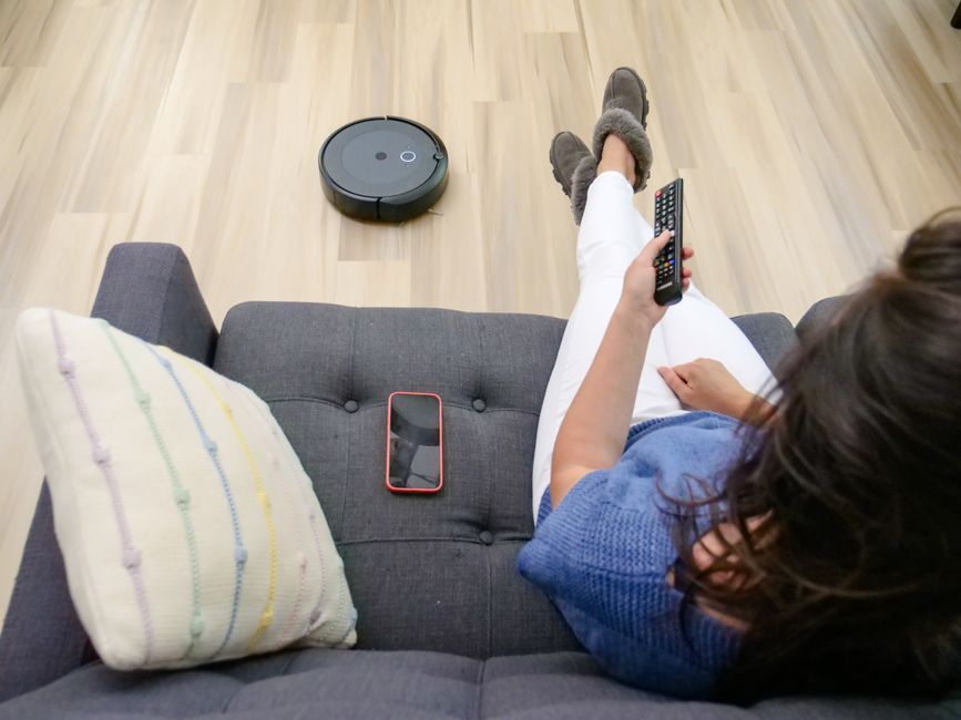 Person relaxing on a sofa controlling a robot vacuum cleaner with a remote.