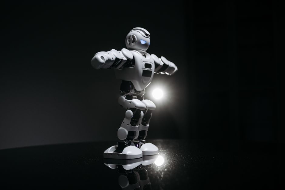 White humanoid robot with glowing eyes standing on a reflective black surface in studio lighting.