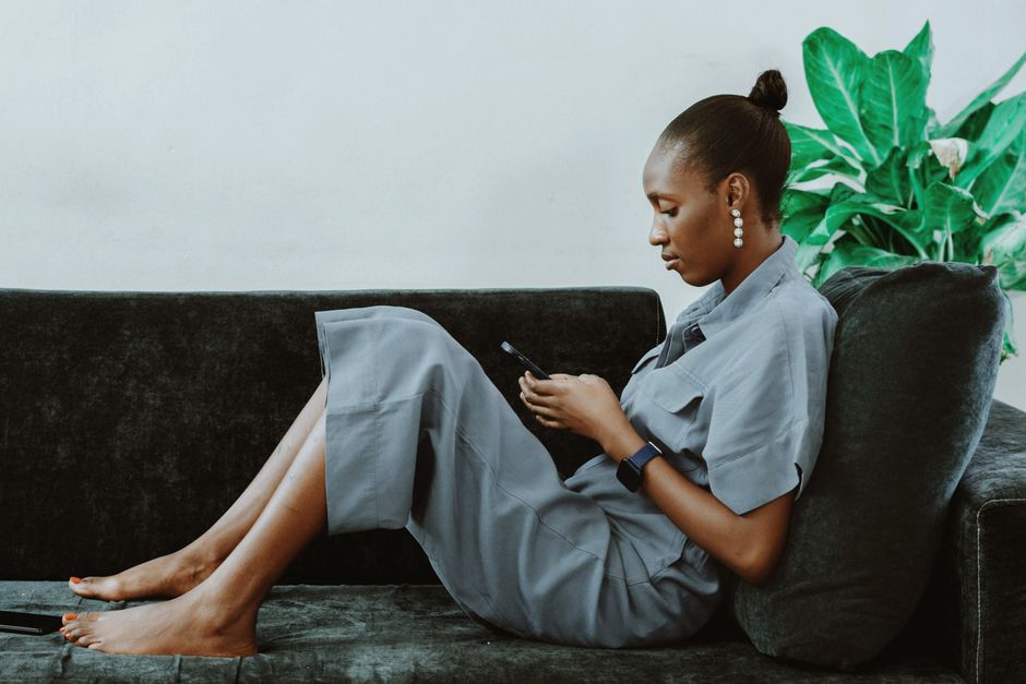Woman lounging on sofa with smartphone, showcasing modern lifestyle and technology.