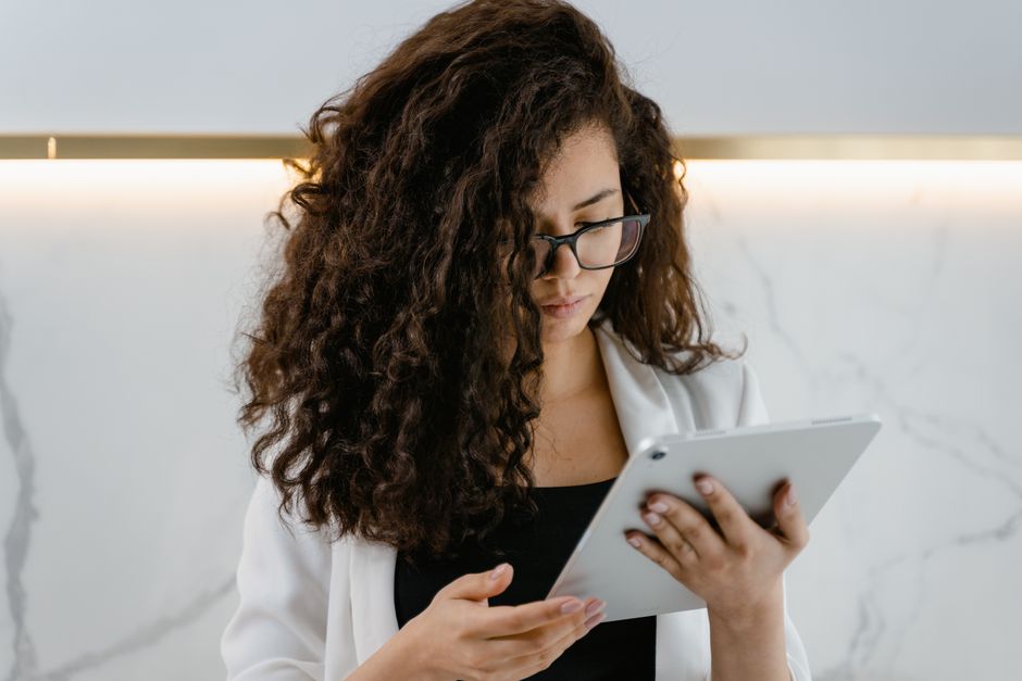 Young woman with curly hair and glasses using a tablet indoors for remote work.
