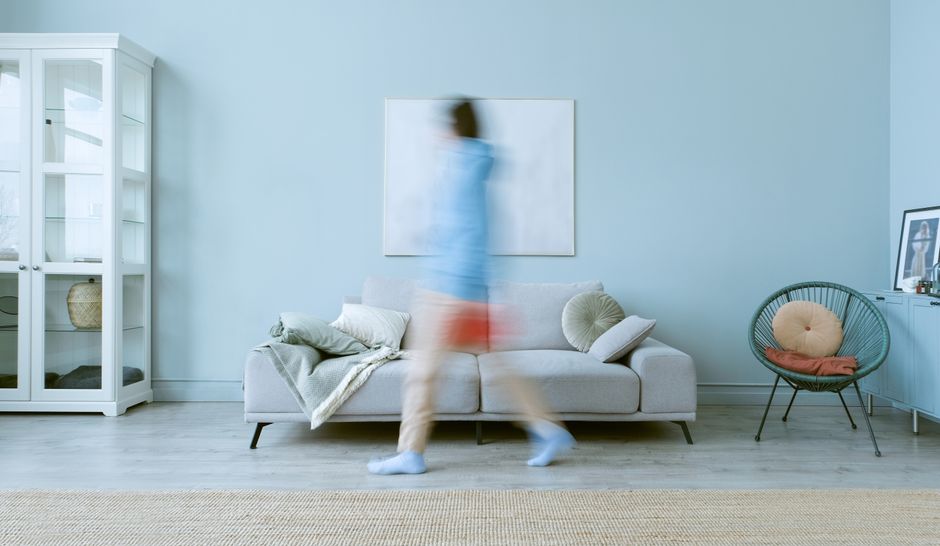 A blurred figure in motion in a minimalist living room setting with a sofa and decor.