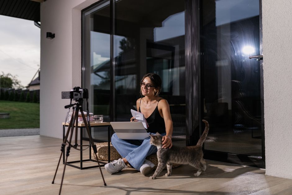 A woman participates in an online class at home, accompanied by her cat, using a laptop.