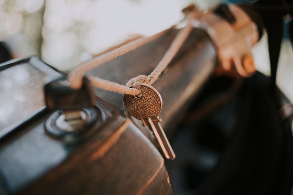 Closeup of metal home key hanging on weathered rope with motorcycle key inserted into slot of vehicle