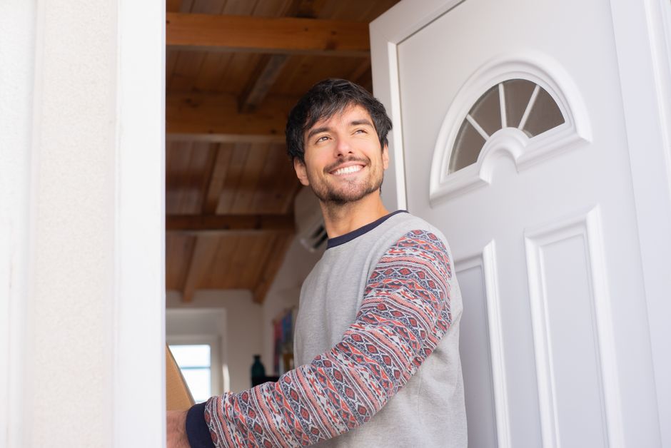 Happy man standing in doorway, smiling brightly. Indoor home setting, warm atmosphere.