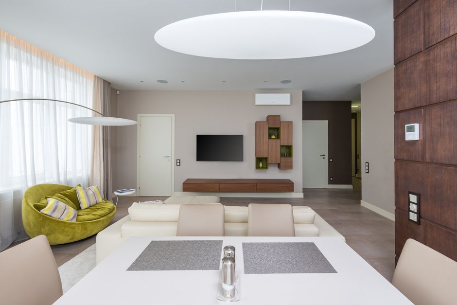 Table with chairs in dining room placed near couch against wall with TV in stylish modern apartment with door at home